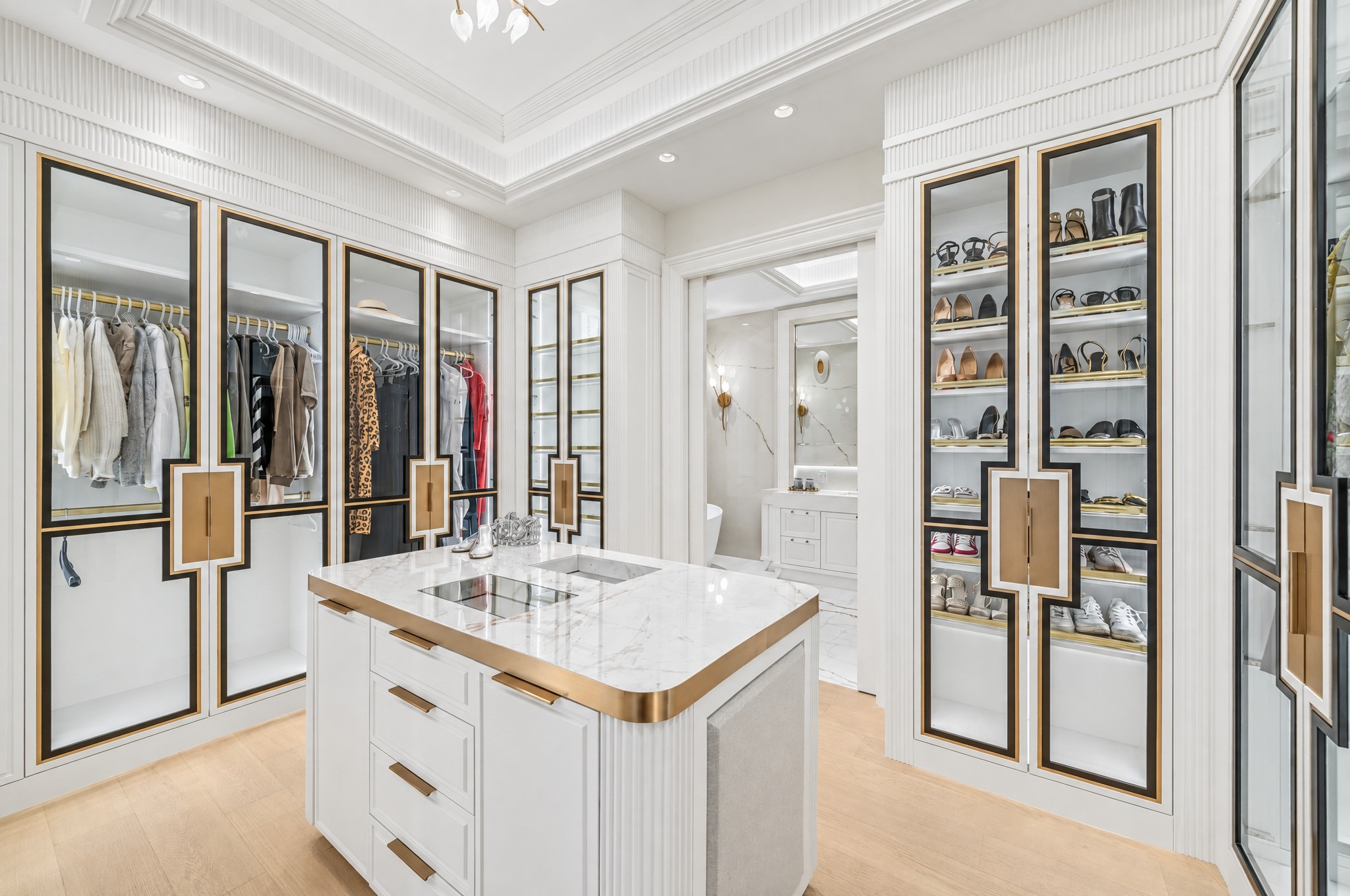 Walk-in dressing room with glass-front wardrobes, brass trim and marble jewellery island