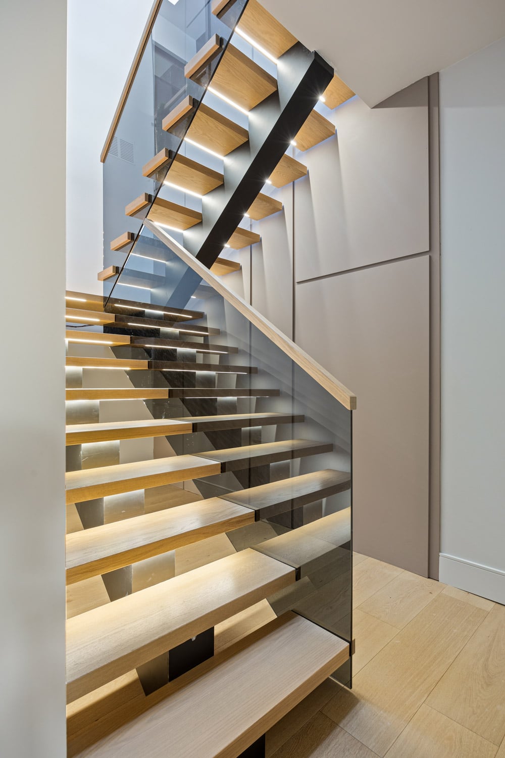 Open-tread oak staircase at 27 Farr Ave with full-height glass panel railings, black steel stringer and LED under-tread lighting
