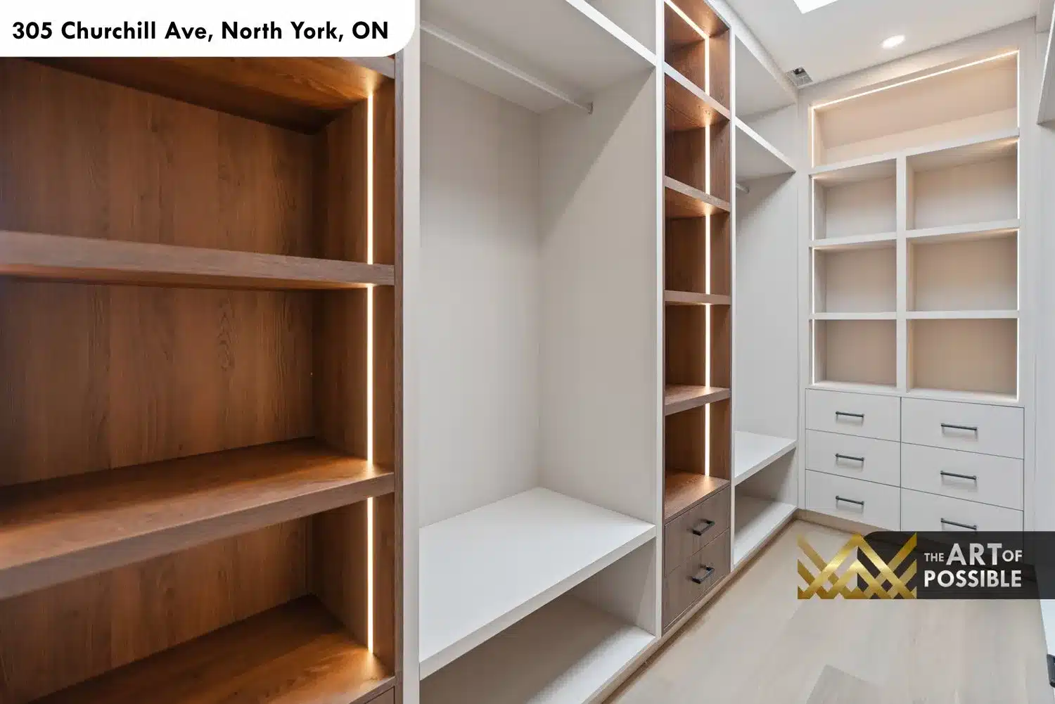 Primary walk-in closet with oak shelving and vertical LED lighting on one side and white built-in drawers and cubbies on the other