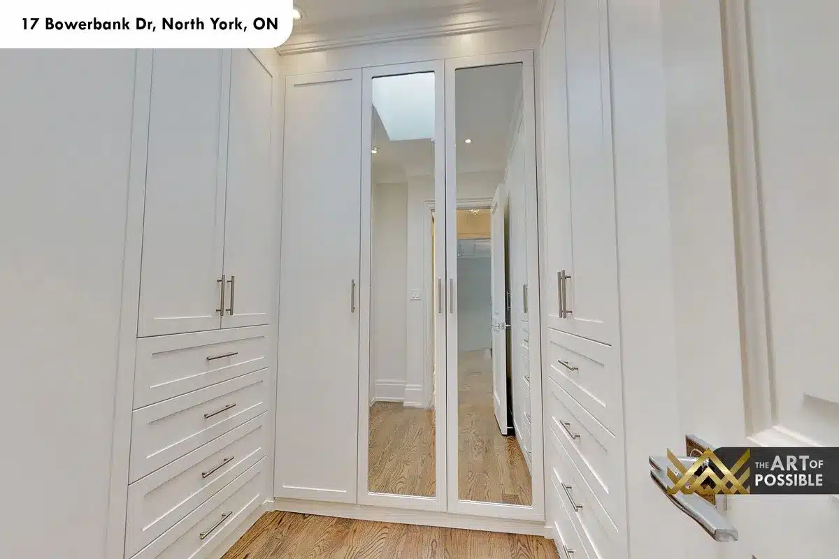 Walk-in closet with floor-to-ceiling white built-in cabinetry, mirrored panels and skylit ceiling