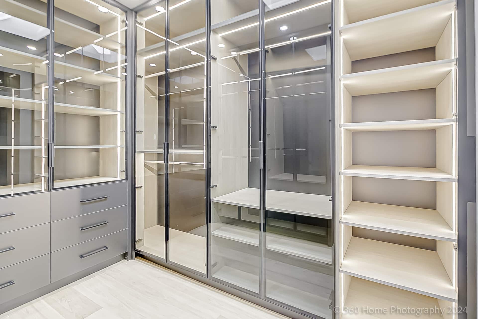 Custom walk-in closet with glass-door wardrobe units and lit interior shelving at 100 Glenvale Blvd