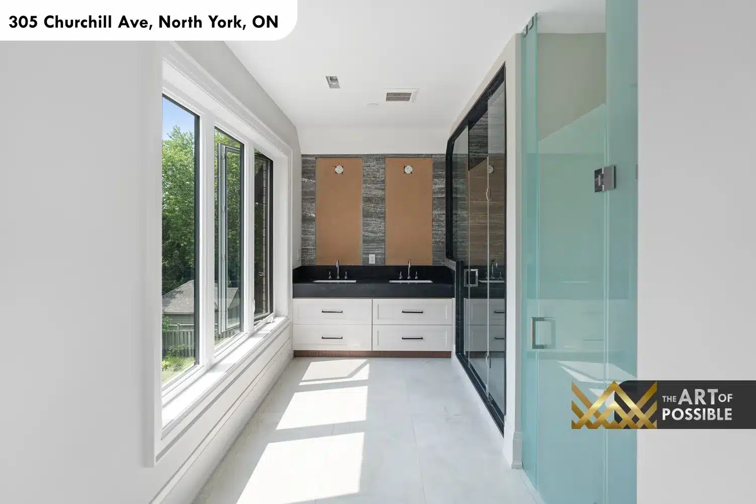 Primary ensuite double vanity with dark quartz countertop, stone accent wall between mirrors and glass shower entry