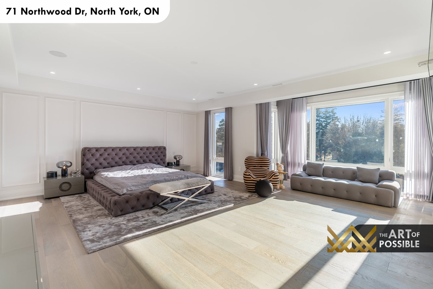Primary bedroom with tufted grey bed, panel moulding wall and floor-to-ceiling rear windows