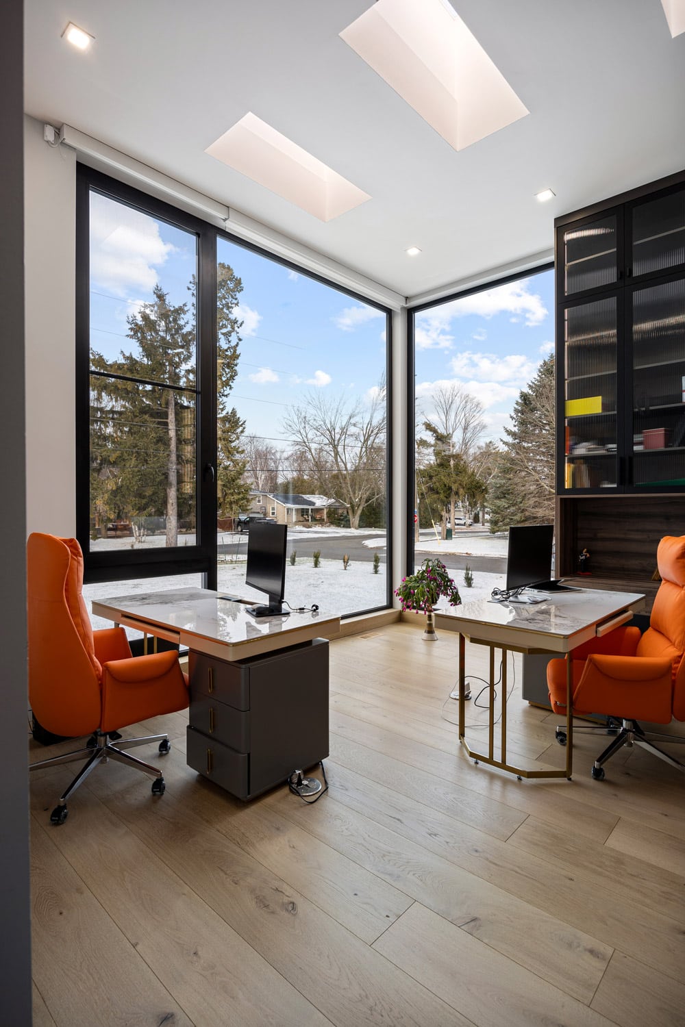 Home office at 27 Farr Ave with corner floor-to-ceiling windows, dual skylights overhead, marble-top desks and dark built-in bookcase