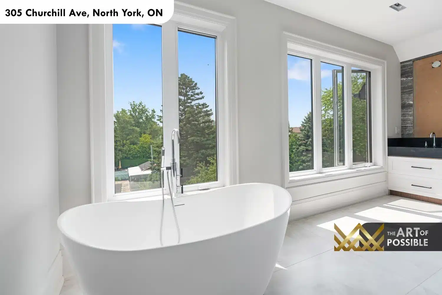 Primary ensuite freestanding oval soaker tub in front of bank of windows with tree canopy views and double vanity beyond