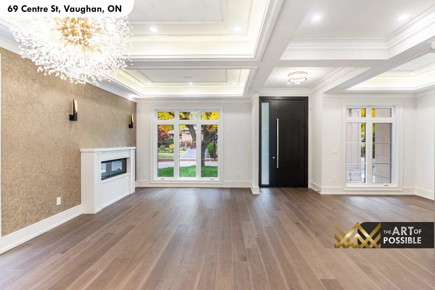 Living area showing coffered tray ceiling, linear fireplace and entry door beyond
