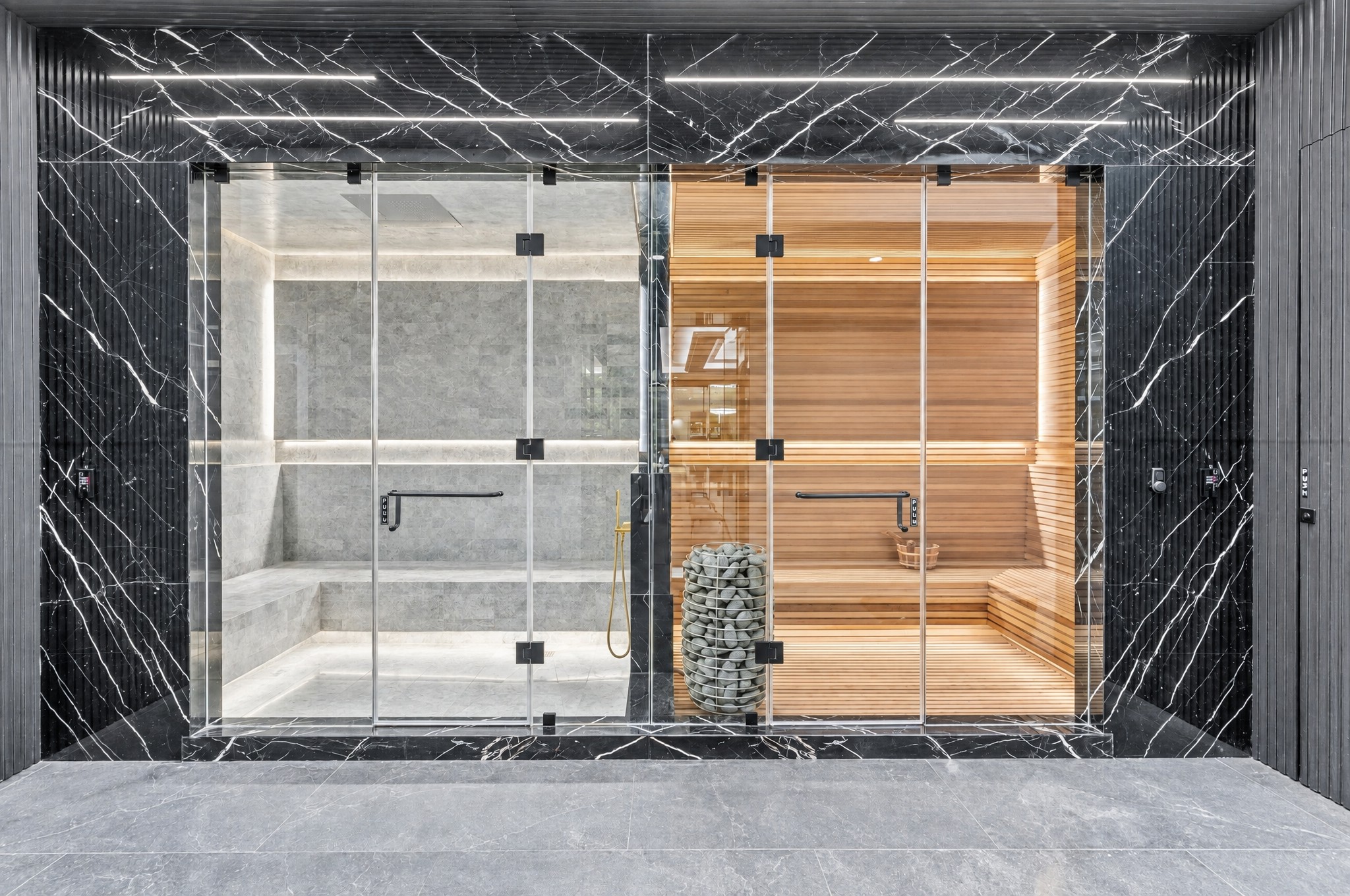 Side-by-side stone steam room and cedar sauna behind glass with black marble surround