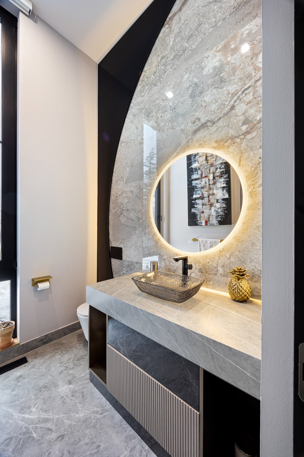 Powder room at 27 Farr Ave with curved arched marble surround, glass vessel sink, round backlit LED mirror and black matte faucet