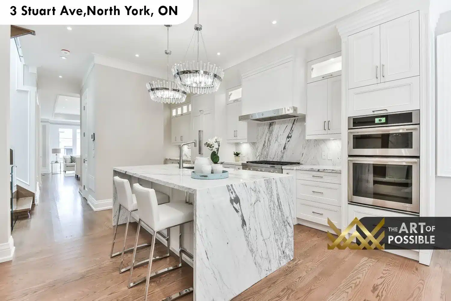 Kitchen showing double stainless wall ovens, gas range, marble backsplash and white barstools at waterfall island