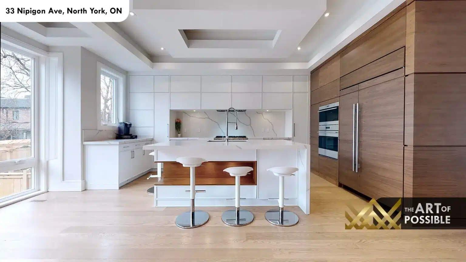 Main kitchen with white waterfall island, walnut refrigerator surround and bar stools