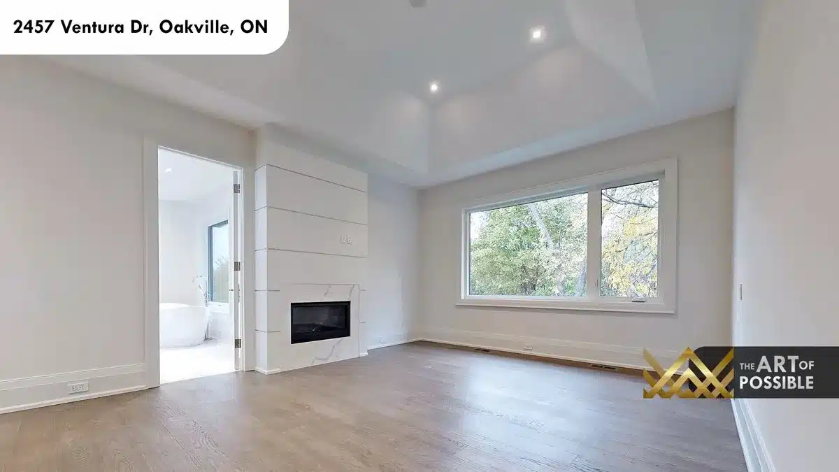 Primary bedroom with marble fireplace tray ceiling and picture window overlooking trees at 2457 Ventura Dr Oakville