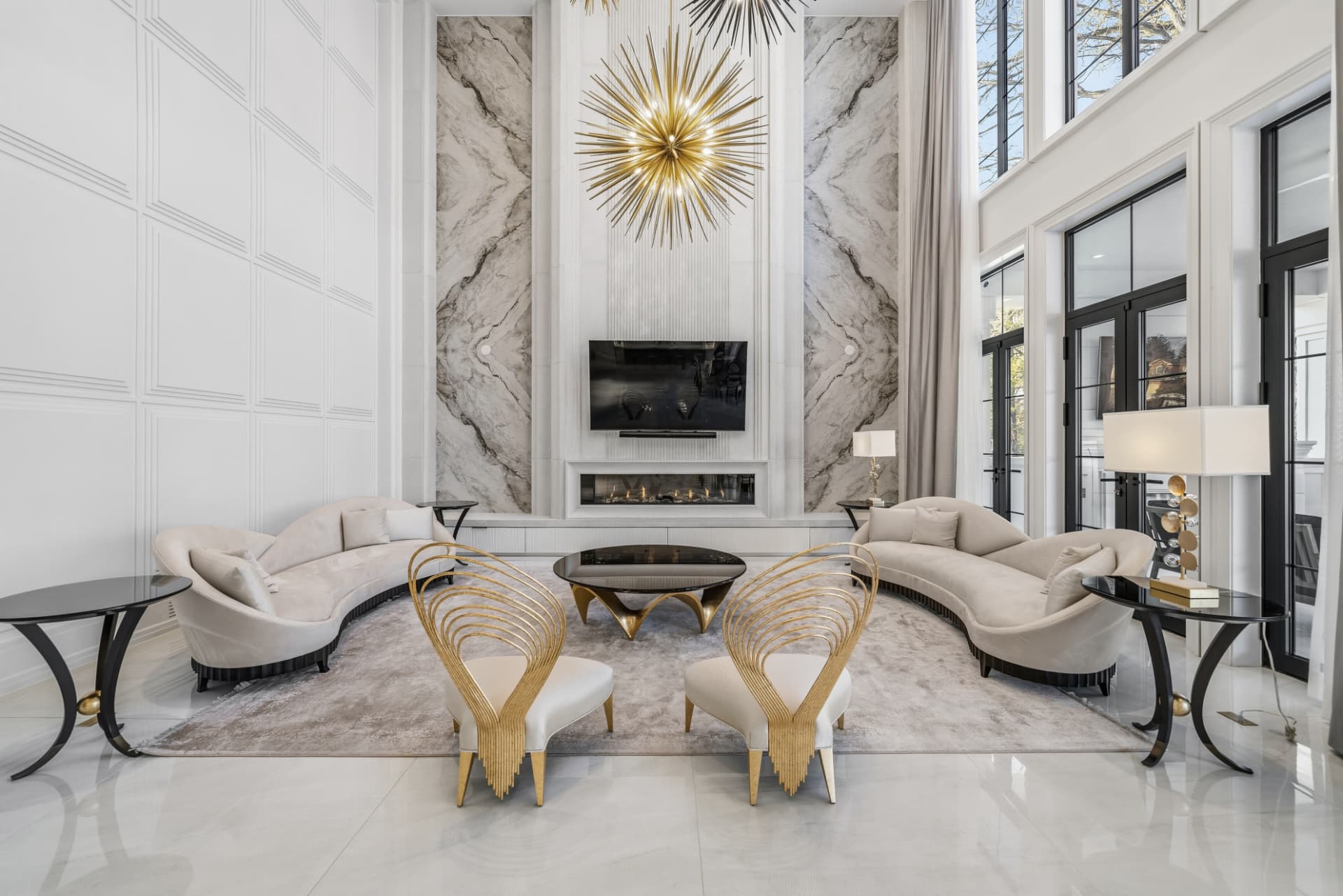 Living room with a golden sunburst chandelier above a linear fireplace, wall-mounted television and bookmatched marble