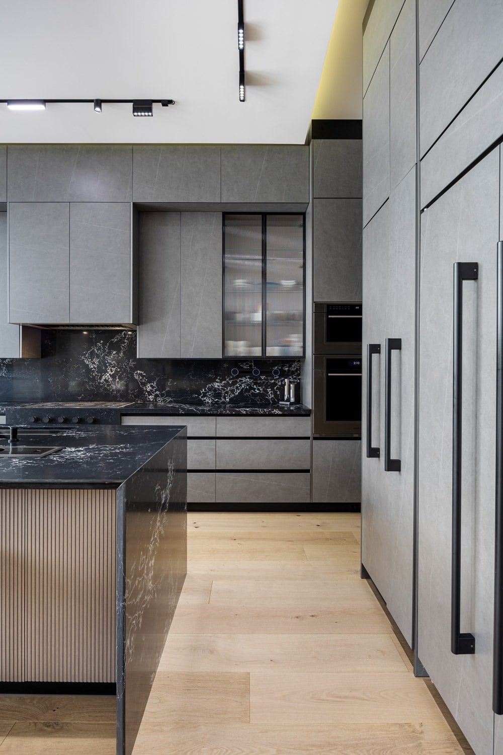 Kitchen detail showing black marble slab backsplash, ribbed glass upper cabinets, integrated panel-front refrigerator and black bar pulls