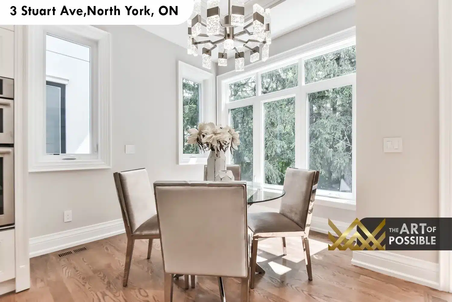 Breakfast nook with corner bay window, chrome-and-crystal chandelier and glass dining table surrounded by lush tree views