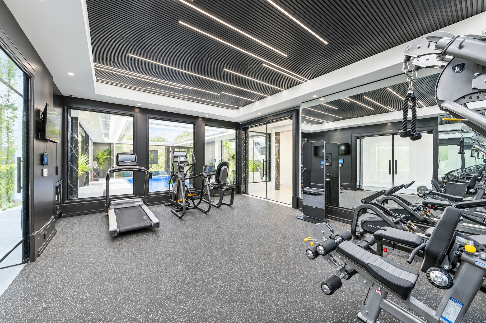 Home gym with slatted LED ceiling, mirrored wall and interior windows overlooking the indoor pool