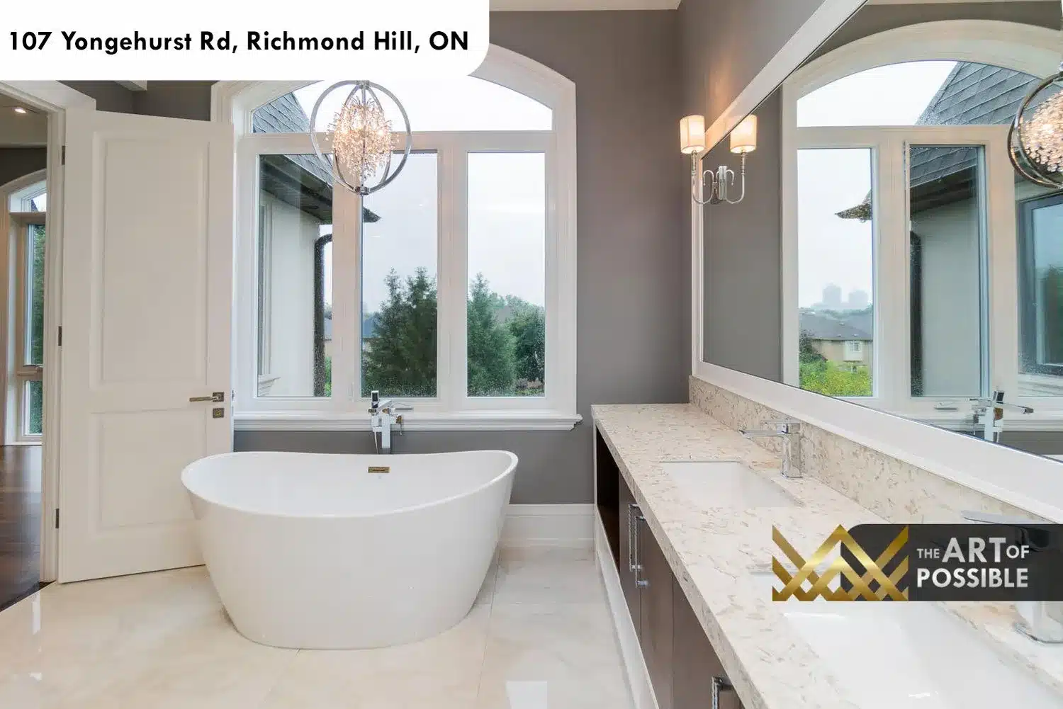 Primary ensuite with freestanding soaker tub, arched window, crystal chandelier and floating double vanity