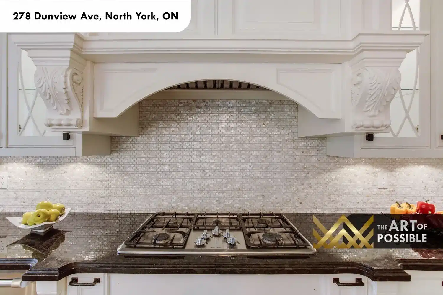 Close-up of the carved kitchen hood with acanthus corbels and mosaic tile backsplash above the cooktop