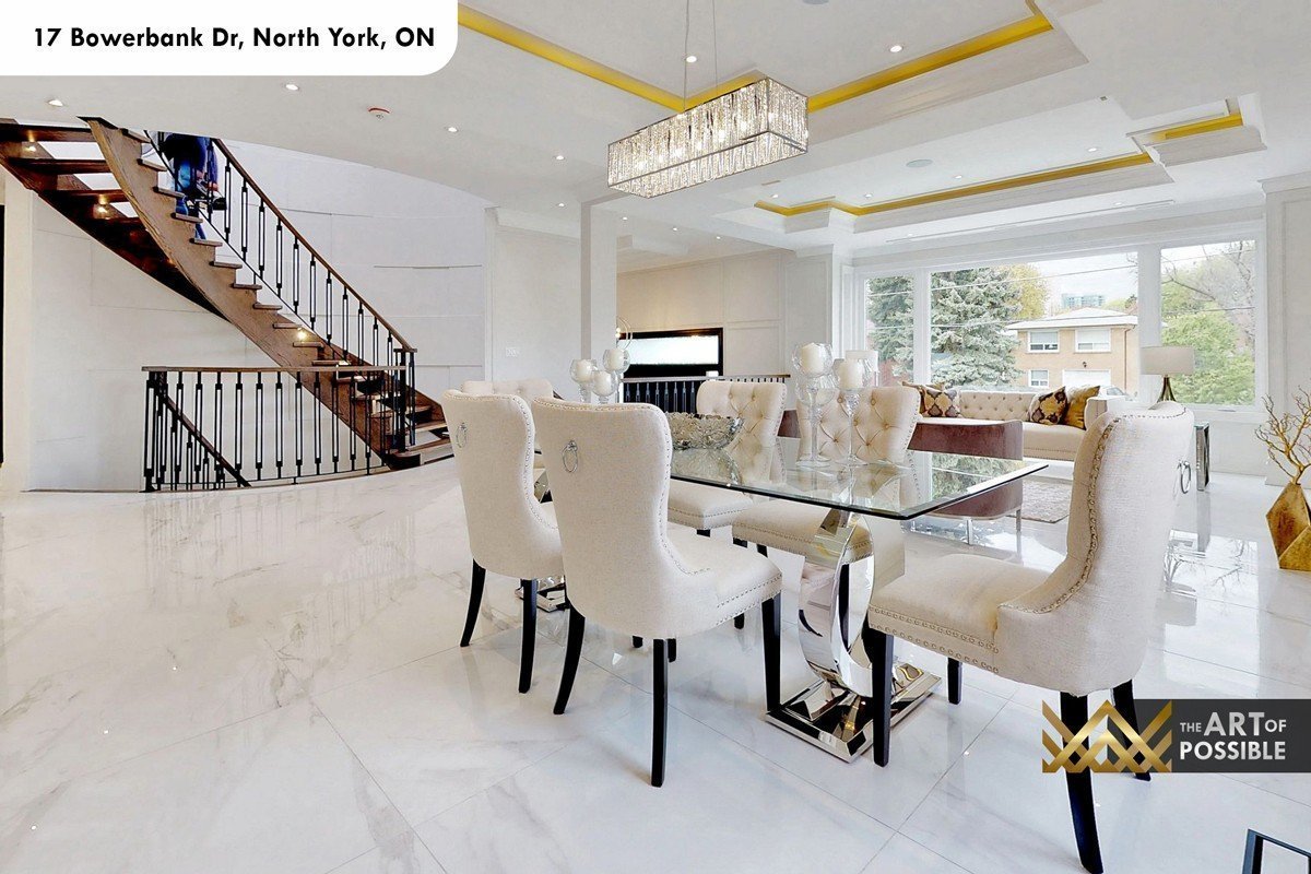 Dining area with crystal rectangular chandelier, glass-top table and curved walnut staircase in background