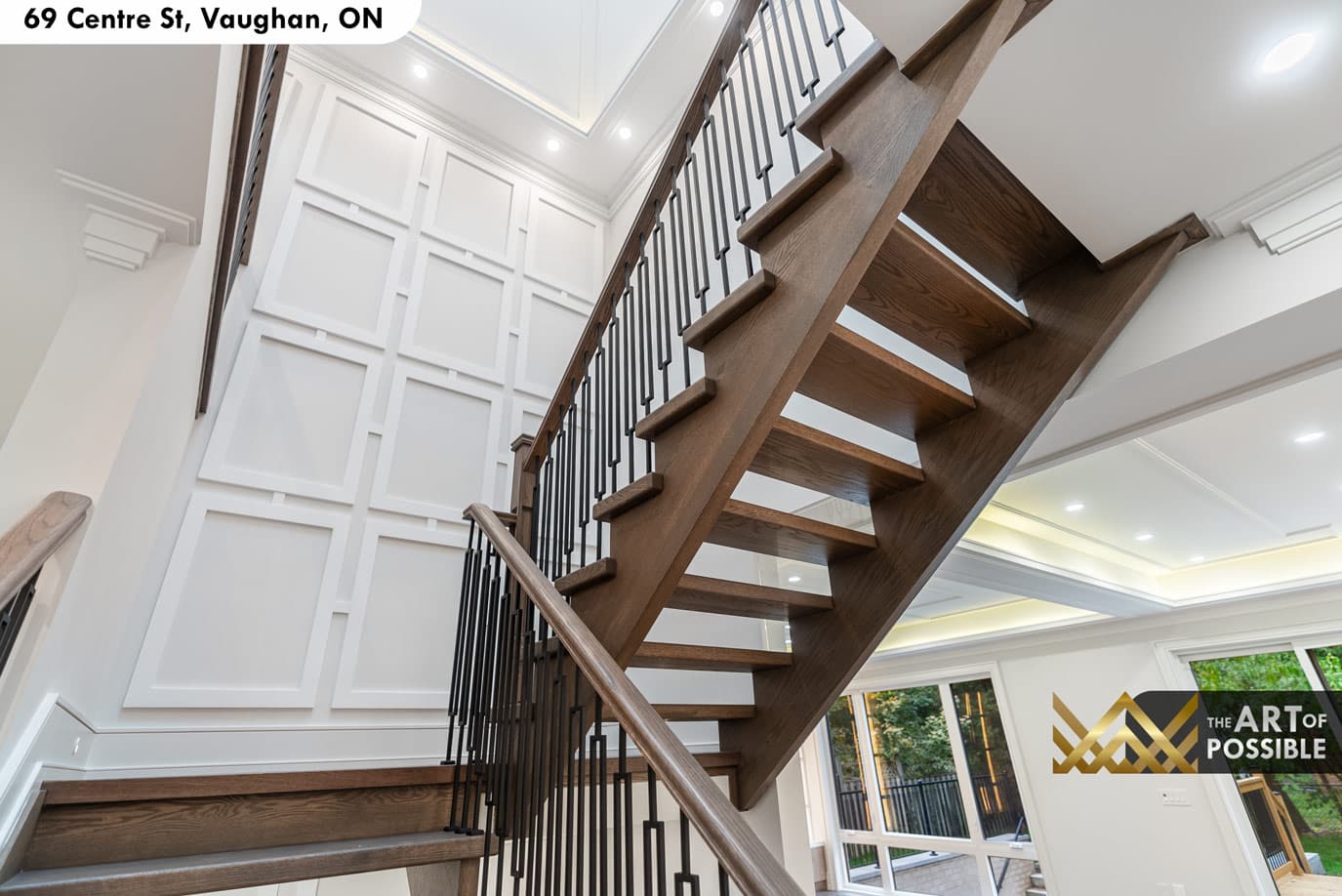 Open-tread dark oak staircase with black iron balusters and wainscoting panel wall