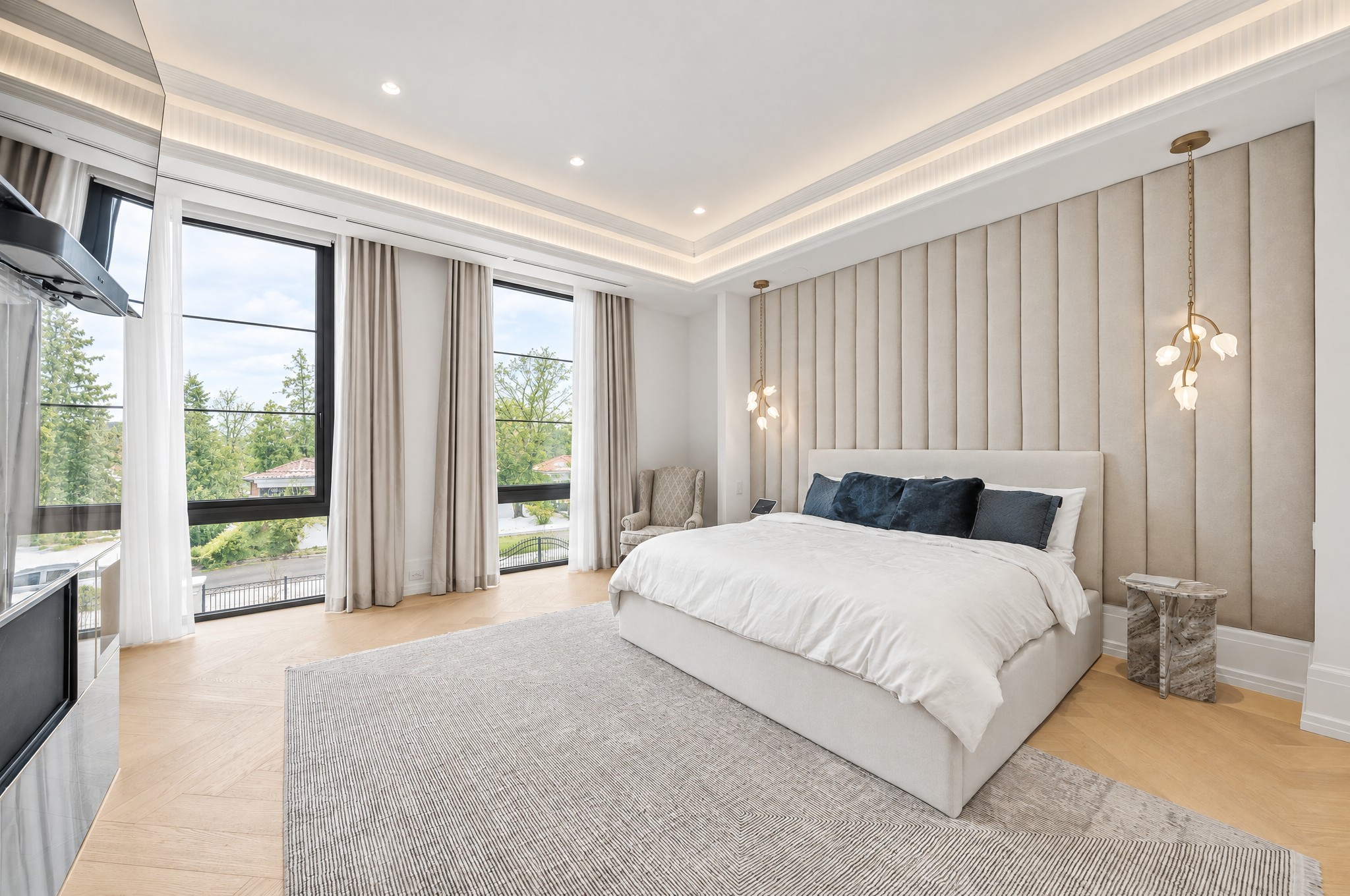 Primary bedroom with channel-tufted upholstered wall, blossom pendants and herringbone oak floors