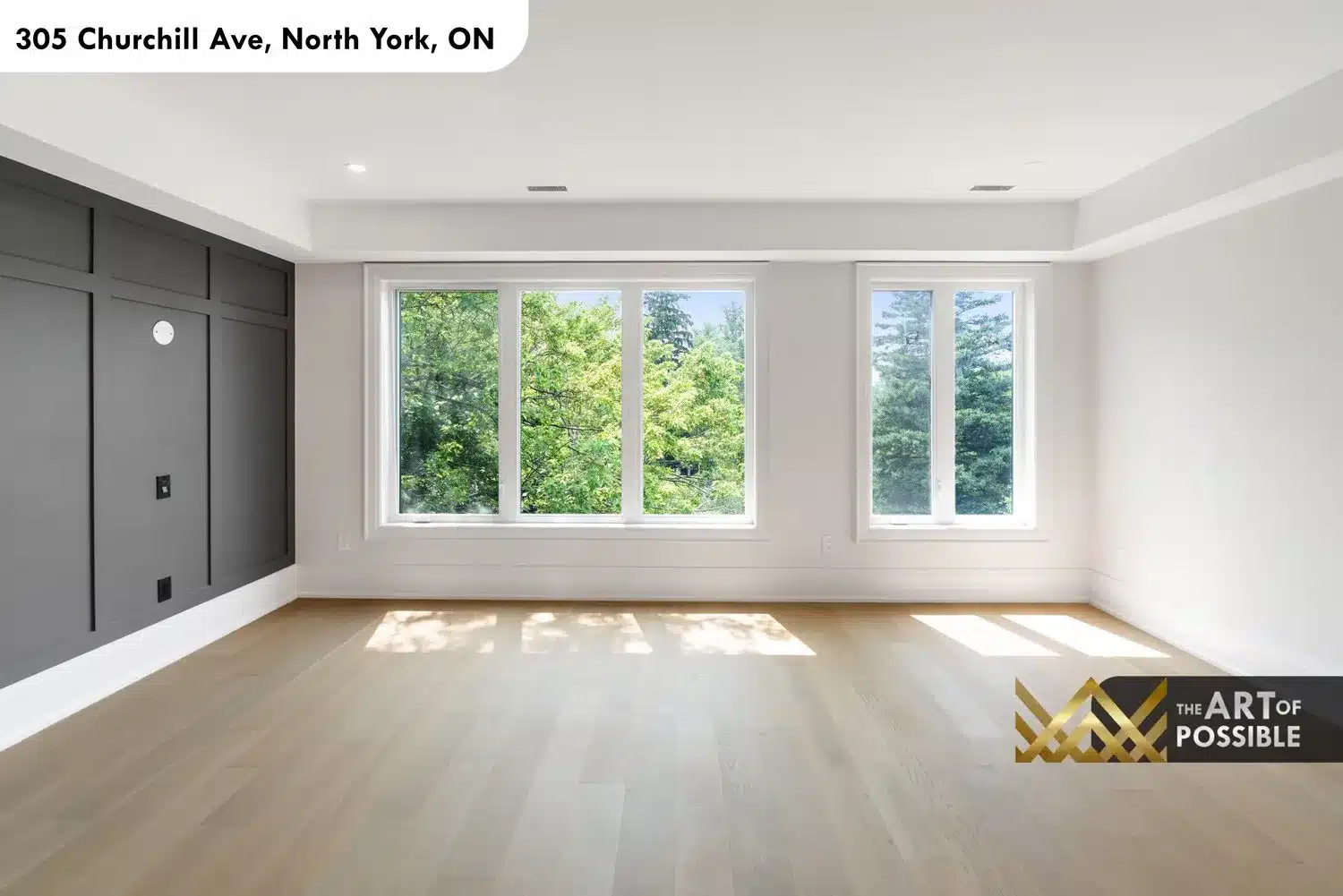 Primary bedroom with charcoal grey panel accent wall and three rear-facing windows overlooking tree canopy