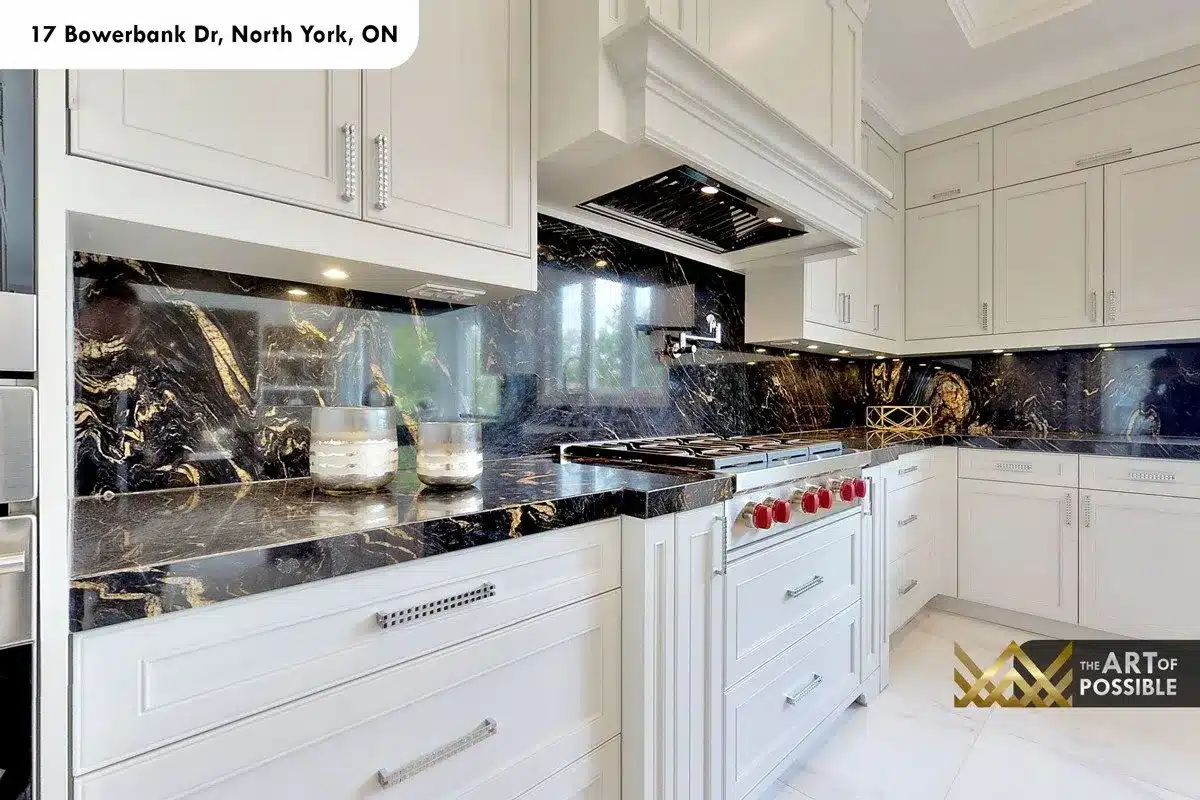 Kitchen detail showing black-and-gold marble full-height backsplash, gas range with red knobs and chrome mirrored range hood