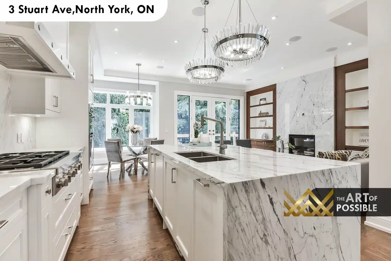 Kitchen looking toward French doors with marble island, crystal chandeliers and walnut shelving niche in family room beyond