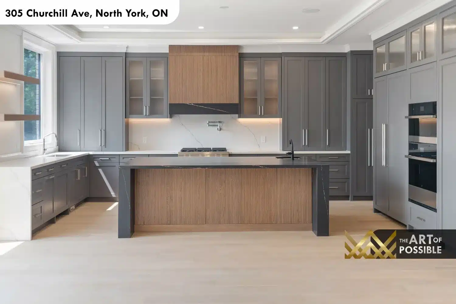 Full kitchen view with grey shaker cabinetry, walnut range hood, dark marble island and double built-in ovens