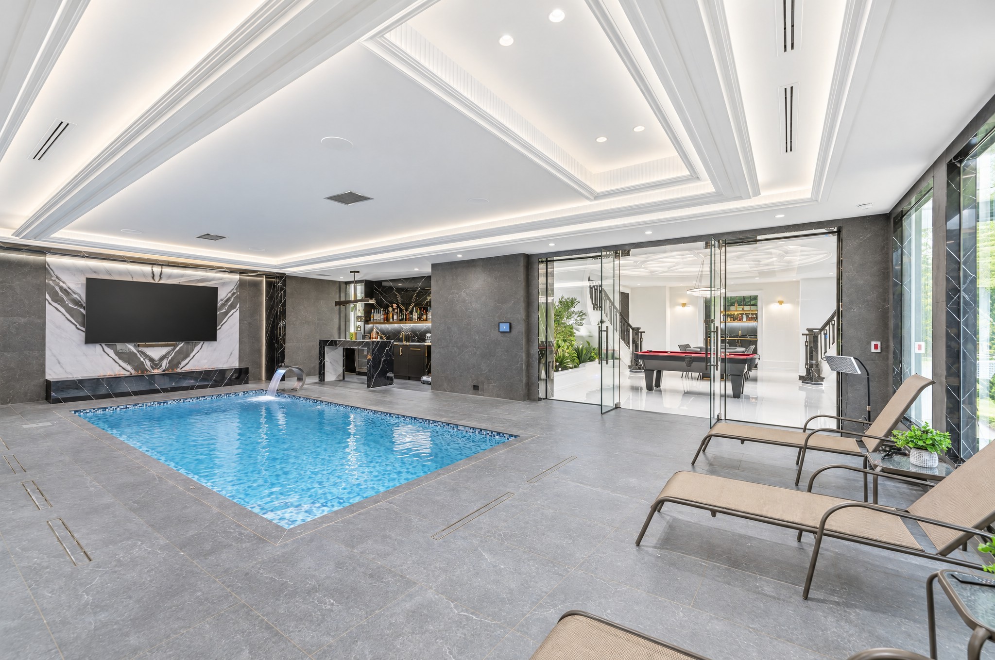 Indoor mosaic tile pool with waterfall spout, marble TV wall and glass doors to billiards area