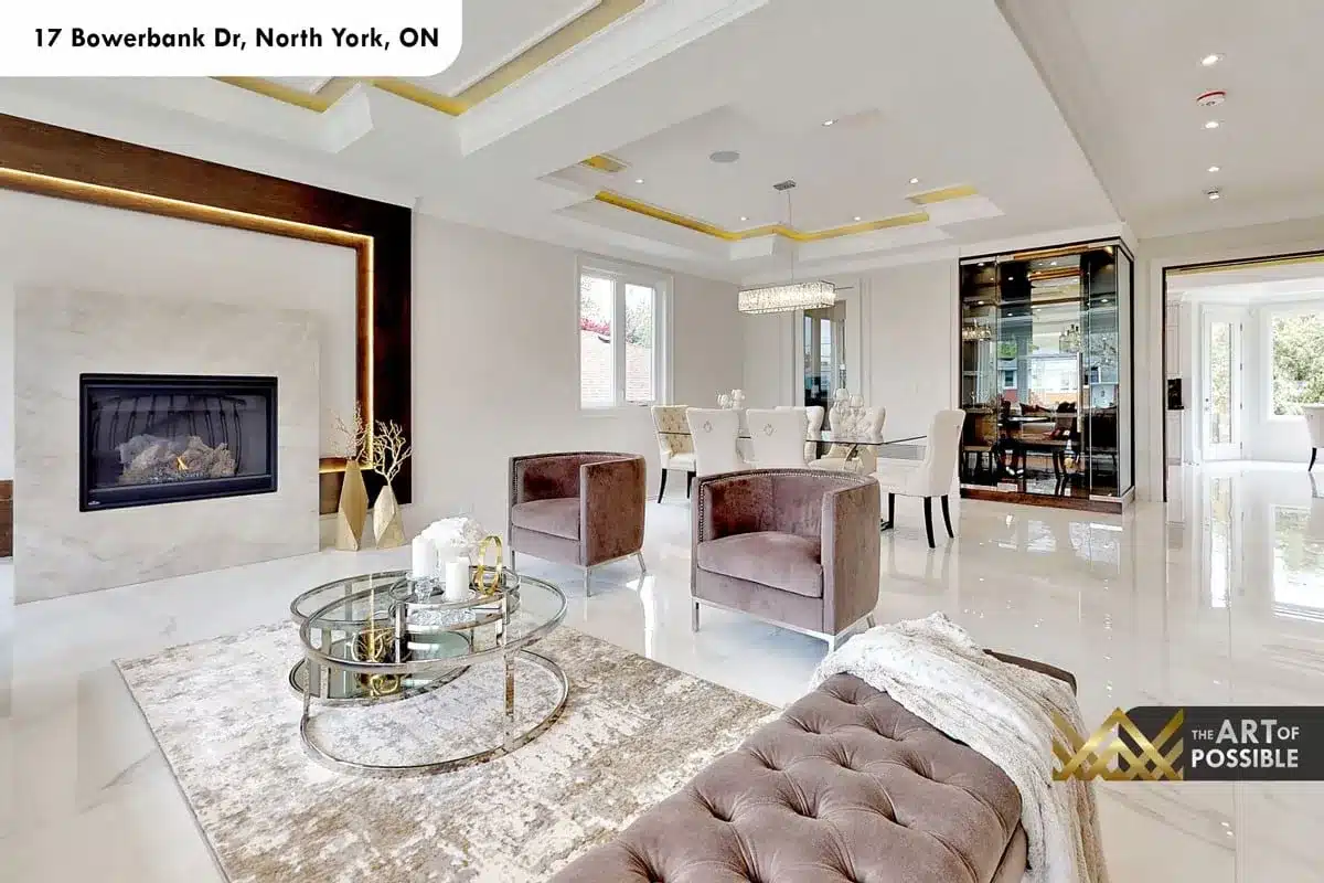 Open-concept living and dining area at 17 Bowerbank Drive showing linear marble fireplace, gold tray ceiling and crystal chandelier