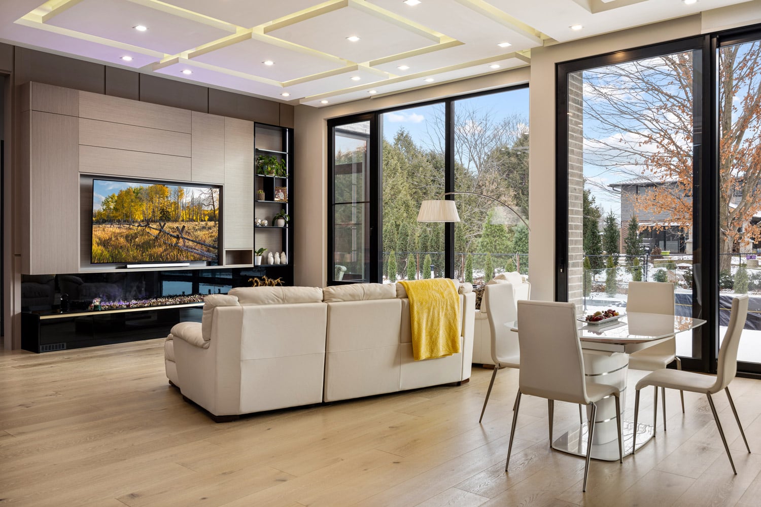 Living and dining area with coffered ceiling LED lighting and views to rear yard through black-framed glass doors